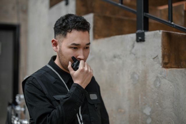 Asian security guard using walkie talkie in an indoor setting, demonstrating communication and alertness.