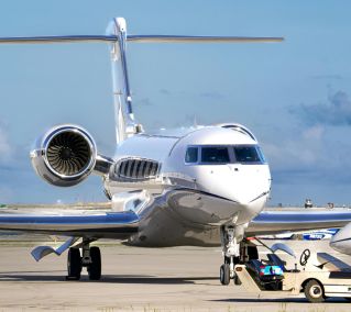 A sleek private jet parked on the tarmac with supporting ground vehicle under a clear blue sky.