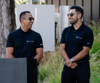 Two adults in black clothing and sunglasses standing by a podium on a sunny day.